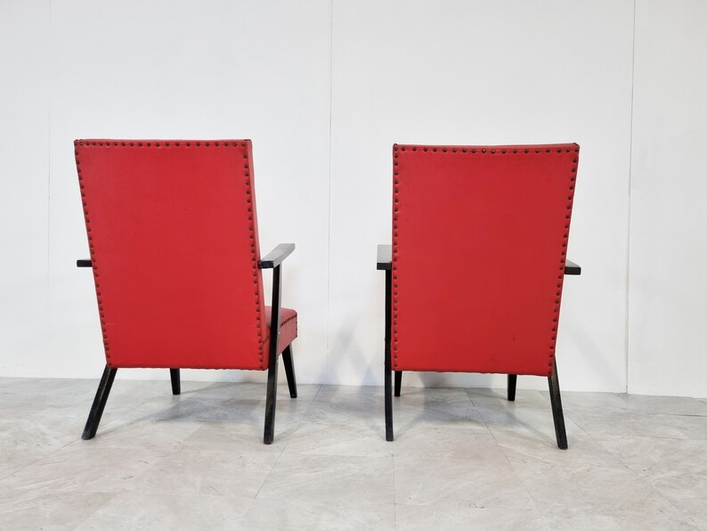 May include: Two red chairs with black wooden frames and black upholstery tacks. The chairs are facing away from the camera.