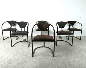May include: Set of six black metal dining chairs with brown fabric seats. The chairs have a curved back and arms.