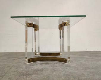 May include: A modern square coffee table with a clear glass top. The table is supported by clear acrylic legs and accented with brass-colored metal bands. The table's dimensions are approximately 30 inches wide and 16 inches high.