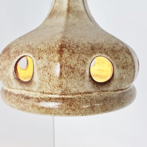 May include: A ceramic lampshade with a light brown glaze and two circular cutouts. The lampshade has a textured surface and a slightly rounded shape.