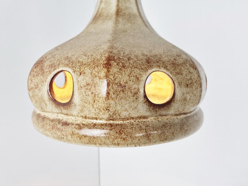 May include: A ceramic lampshade with a light brown glaze and two circular cutouts. The lampshade has a textured surface and a slightly rounded shape.