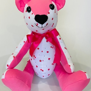 May include: A pink and white teddy bear with a pink bow. The bear has a white body with pink polka dots and a pink face. The bear is sitting on a white surface.