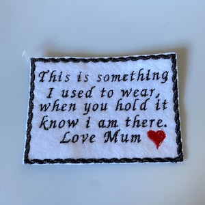May include: A white embroidered patch with black text that reads "This is something I used to wear, when you hold it know I am there. Love Mum." A small red heart is embroidered below the text. The patch has a black border.
