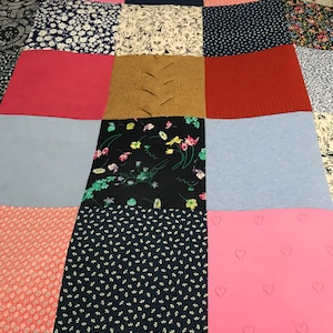 May include: A patchwork quilt featuring a range of fabrics in various colours and patterns, including floral, polka dot, and plain colours. The quilt is composed of squares and rectangles, with the seams clearly visible.
