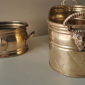 Peut inclure: Deux pots ovales en laiton avec des poignées décoratives. Le plus petit pot a un motif de coquille. Le plus grand pot a un motif de tête de lion.
