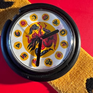 以下が含まれることがあります： 黒い持ち手と「But First, Coffee」の太字の黒い文字が入った白いセラミックマグ。マグカップはぼやけた背景に置かれ、居心地の良い環境を示唆しています。