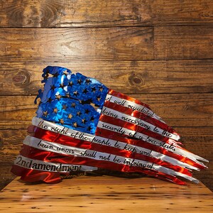 May include: A distressed metal American flag with the 2nd Amendment text: "A well regulated Militia, being necessary to the security of a free State, the right of the people to keep and bear Arms, shall not be infringed."