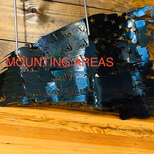 May include: A black metal American flag with a distressed look. The flag is mounted on a wooden wall and has the words "We the People" inscribed on it. The words "Mounting Areas" are written in red text at the top of the image.
