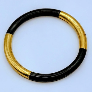 May include: A circular bracelet with a segmented design. The bracelet is primarily black with gold-colored sections. The gold sections appear to be metallic, while the black sections have a smooth, possibly enameled, finish. The bracelet is shown against a white background.