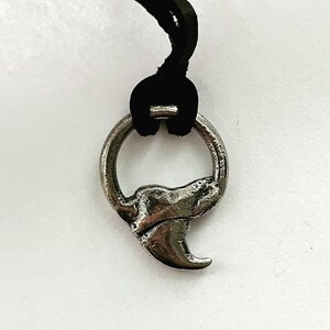 May include: A silver-colored pendant with a claw design, attached to a black cord. The pendant has a circular ring at the top and a detailed claw shape at the bottom. The background is white.