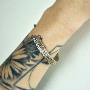 May include: A silver textured cuff bracelet with a hammered finish.