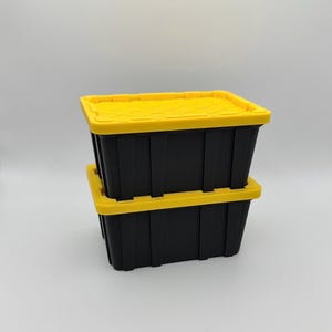 May include: Two black storage bins with bright yellow lids are stacked on top of each other. The bins are rectangular and made of plastic. The lids have a textured surface. The background is a plain, light gray.