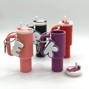 May include: Four colorful, personalized, plastic water bottles with attached keychains. Each bottle has a different color and a letter on the keychain. The bottles are pink, purple, black, and red.