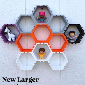 May include: A modular wall-mounted shelving unit composed of seven interlocking hexagonal compartments in gray, orange, black, purple, and white. Small toy figures are placed inside four of the shelves. The text New Larger Sizes is visible.