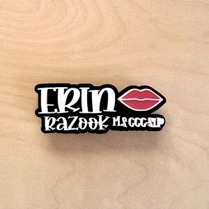 Puede incluir: Una pegatina en blanco y negro con el nombre "ERIN" y las palabras "RAZOOK MS CCC SLP" en cursiva. Un gr&aacute;fico de labios rojos est&aacute; en el lado derecho de la pegatina.