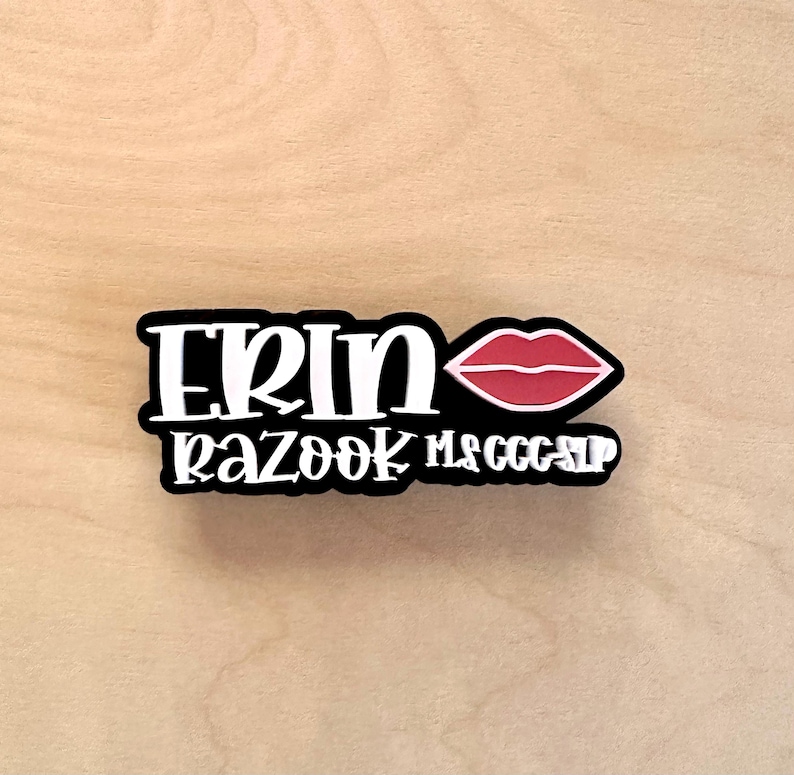 Puede incluir: Una pegatina en blanco y negro con el nombre "ERIN" y las palabras "RAZOOK MS CCC SLP" en cursiva. Un gr&aacute;fico de labios rojos est&aacute; en el lado derecho de la pegatina.