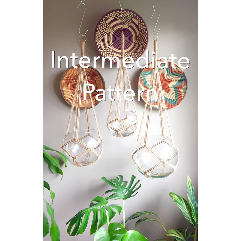 May include: Three macrame plant hangers made with natural twine, hanging from the ceiling. The hangers are in various stages of completion, with one finished and two in progress. The hangers are hanging in front of a wall with three woven baskets.