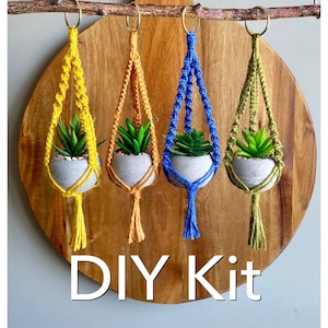 May include: DIY kit for making macrame plant hangers. The kit includes four different colored cords: yellow, orange, blue, and green. Each hanger is decorated with a small potted plant.