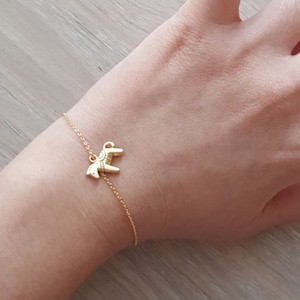 May include: A gold chain bracelet with a small gold horse charm. The bracelet is on a person's wrist.
