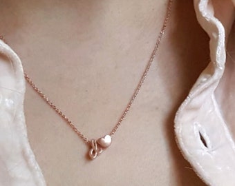 Könnte beinhalten: Eine zarte Halskette aus Roségold mit zwei kleinen Herzanhängern. Die Kette wird von einer Person mit langen blonden Haaren und einem rosa Hemd getragen.