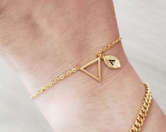 Könnte beinhalten: Ein goldenes Kettenarmband mit einem Dreiecksanhänger und einem Blattanhänger mit dem Buchstaben A.