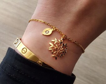 May include: A gold chain bracelet with a delicate leaf charm and a small circle charm. The bracelet is on a person's wrist.