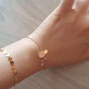 May include: A gold chain bracelet with a pineapple charm and a small leaf charm with the letter "P" on it.