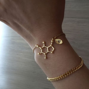May include: A gold chain bracelet with a charm in the shape of a chemical molecule and a small gold charm with the letter A.