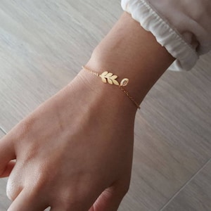May include: A delicate gold chain bracelet with a small leaf charm. The bracelet is on a person's wrist.