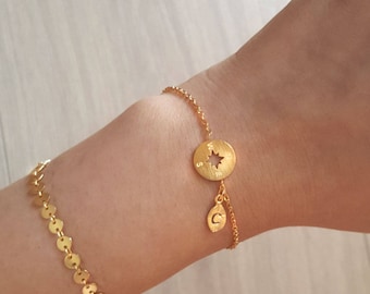 May include: Gold bracelet with a compass charm and a letter 'C' charm. The compass charm has a star cut out in the center.
