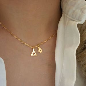 May include: A gold necklace with a small triangle pendant and a charm with the letter 'C'.