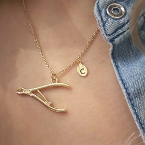 May include: Gold necklace with a nail clipper charm and a small oval charm with the letter 'C' engraved on it.