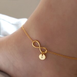 May include: Gold infinity anklet with a small round charm with a letter 'S' on it.