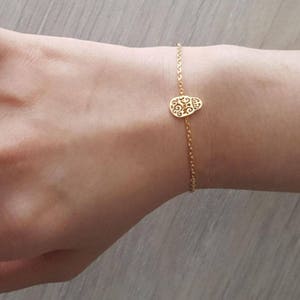 May include: A gold chain bracelet with a delicate, ornate skull charm. The bracelet is on a person's wrist.