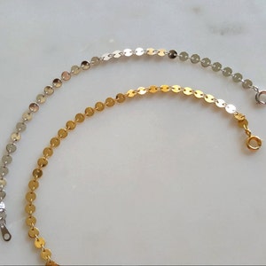 May include: Two delicate chain bracelets, one silver and one gold, with small round links. The bracelets are on a white surface.
