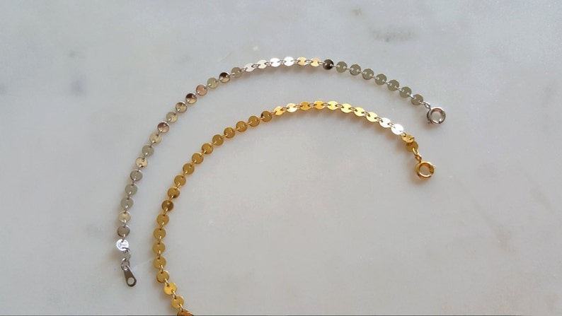 May include: Two delicate chain bracelets, one silver and one gold, with small round links. The bracelets are on a white surface.