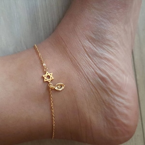 May include: A gold ankle bracelet with a star of David charm and a hamsa hand charm.