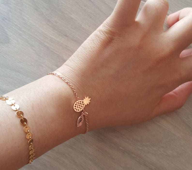 May include: A gold chain bracelet with a pineapple charm and a small leaf charm with the letter "P" on it.