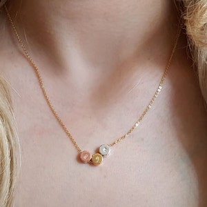 Könnte beinhalten: Eine goldene Kettenkette mit drei kleinen runden Anhängern. Die Anhänger sind in verschiedenen Farben: Gold, Roségold und Silber.