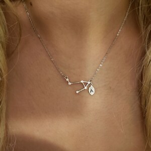 May include: A silver necklace with a constellation pendant and a small charm with the letter 'A' on it.