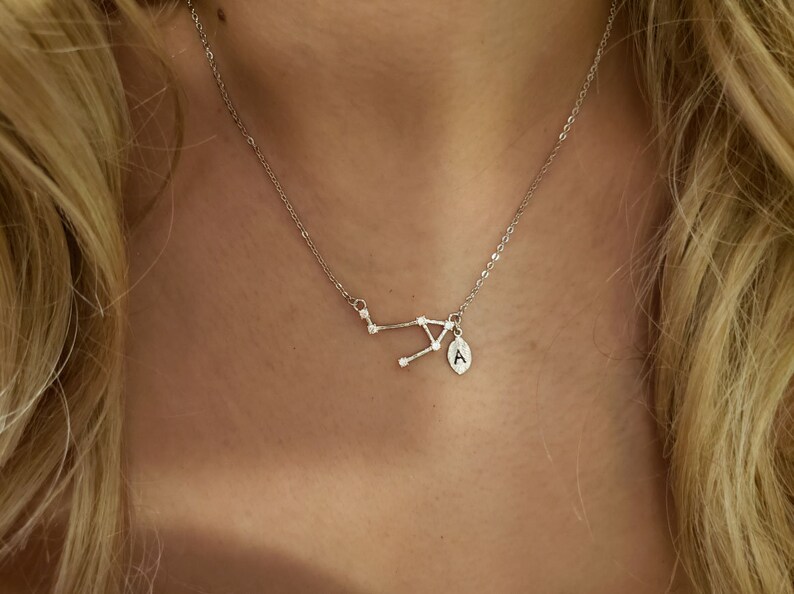 May include: A silver necklace with a constellation pendant and a small charm with the letter 'A' on it.
