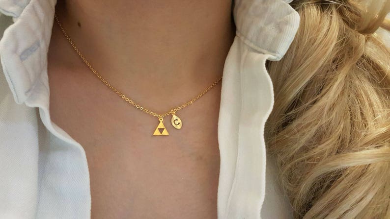 May include: A gold necklace with a small triangle pendant and a charm with the letter 'C' on it.