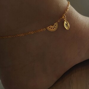 May include: Gold ankle chain with a watermelon slice charm and a leaf charm with the letter K.