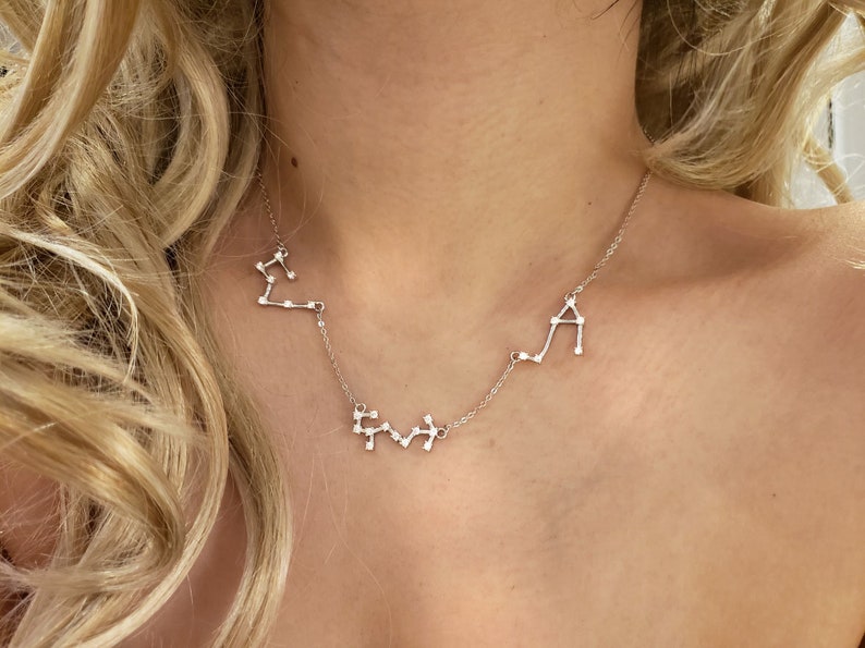 May include: A silver necklace with three constellation pendants. The constellations are Libra, Gemini, and Aquarius.