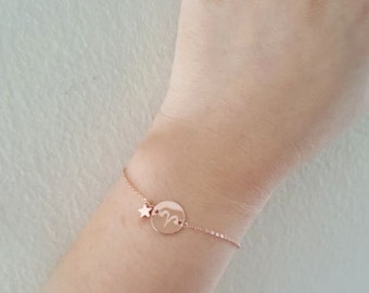 May include: A rose gold chain bracelet with a round charm featuring the zodiac symbol for Aries. A small star charm hangs from the bracelet.