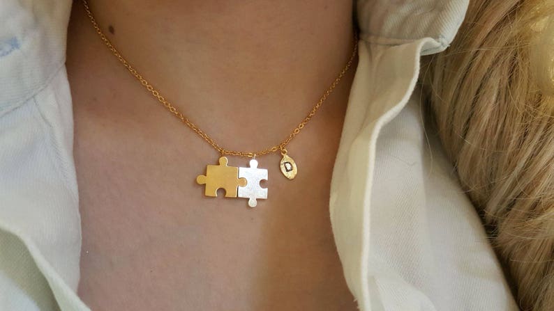 May include: A gold chain necklace with a two-piece puzzle pendant and a small charm with the letter 'D' on it.