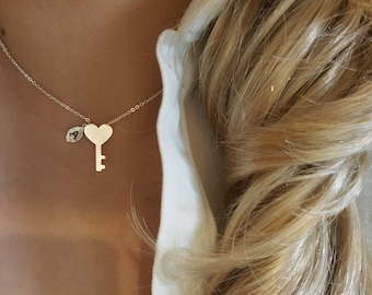 Könnte beinhalten: Eine silberne Halskette mit einem herzförmigen Schlüsselanhänger und einem kleinen Blatt-Anhänger mit dem eingravierten Buchstaben "A".