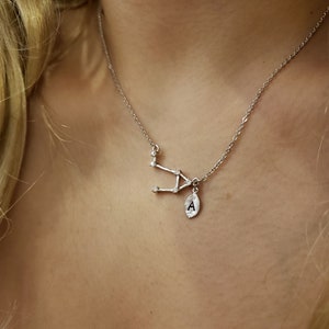 May include: A silver necklace with a constellation pendant and a small charm with the letter 'A' on it.