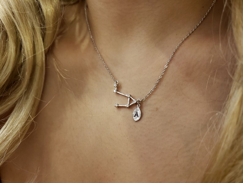 May include: A silver necklace with a constellation pendant and a small charm with the letter 'A' on it.