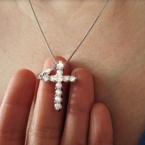 Puede incluir: Un collar de cadena de plata con un colgante de cruz engastado con diamantes.